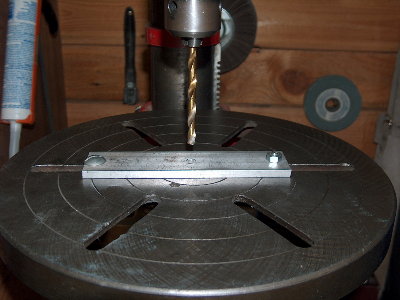 Bolt the piece of flat bar to the drill press. Using the same drill bit you used to drill the hole, VERY carefully line up the bit with the hole. Tighten things down, double check alignment.