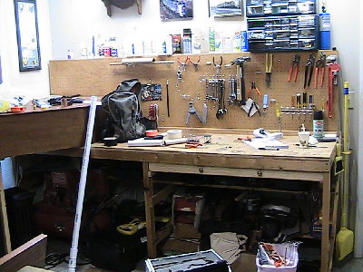main work bench with a tool wall and many power tools and an air compressor underneath